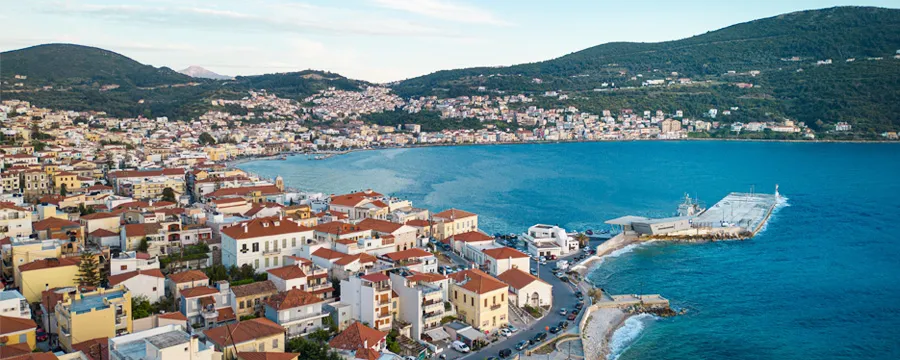Παραθαλάσσια πόλη της Σάμου με κτίρια με κόκκινες στέγες και γαλάζια νερά κάτω από μερικώς συννεφιασμένο ουρανό.