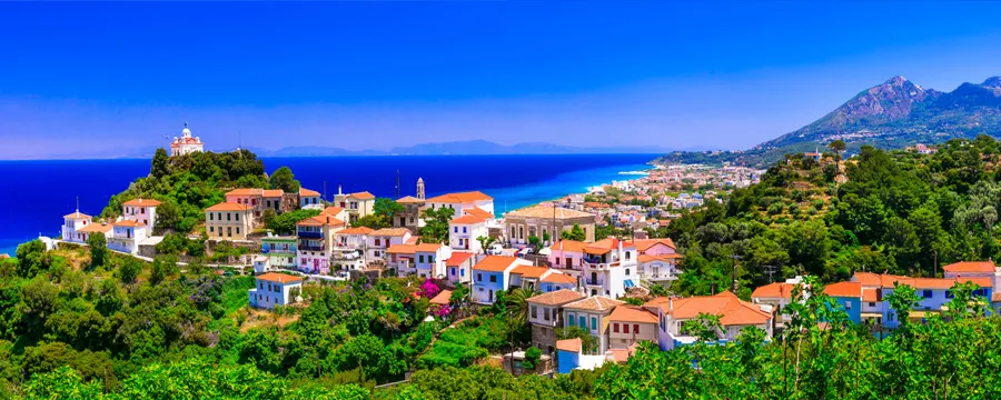 Σάμος, Ελλάδα παραθαλάσσια πόλη με λευκά σπίτια, πράσινους λόφους, μπλε θάλασσα και καθαρό ουρανό.