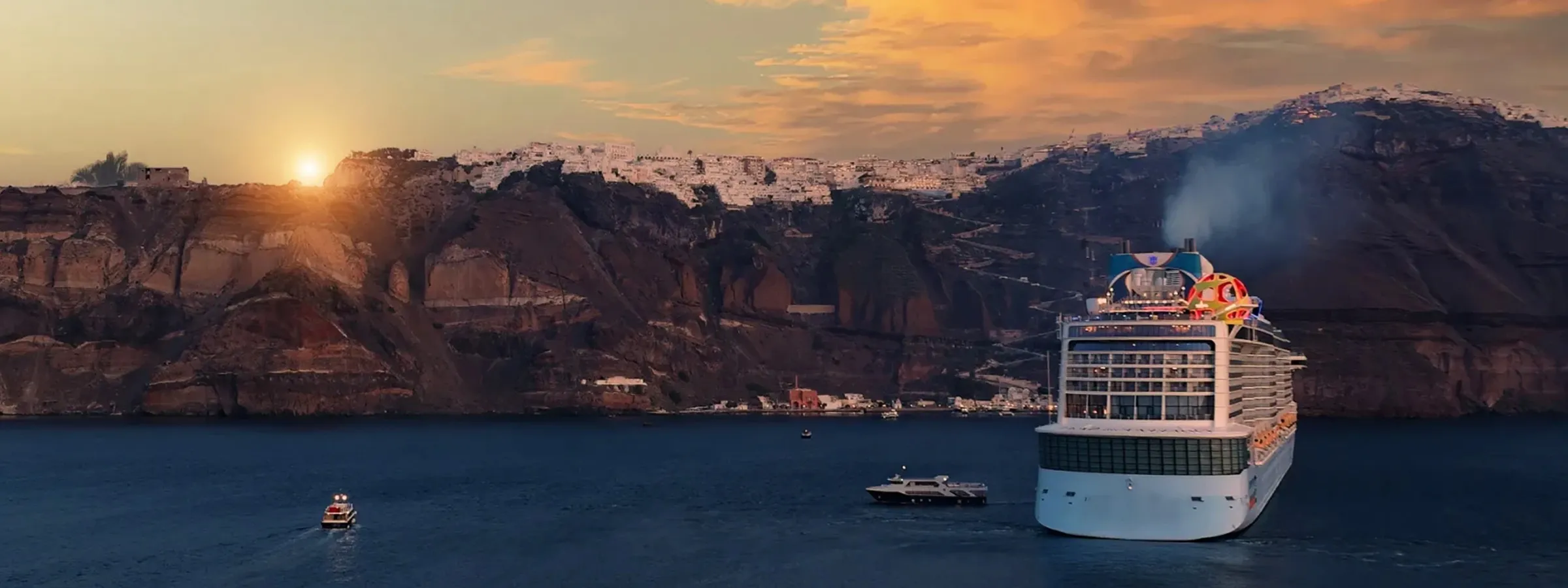 A cruise ship sails near Santorini’s cliffside village at sunset, with boats floating on calm blue waters.