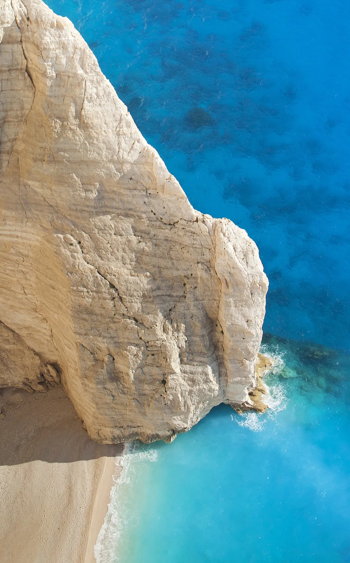 Towering white limestone cliffs contrast with the turquoise waters and sandy beach of Zakynthos, Greece.
