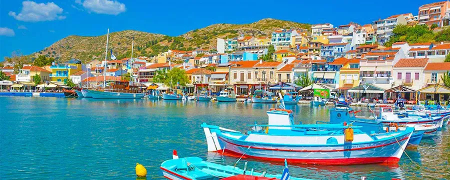 Samos, Yunanistan kıyısında rengarenk evler ve teknelerle süslü sakin bir liman manzarası.