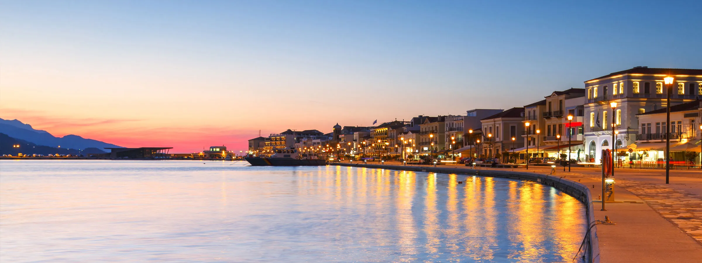 Samos Adası’nın sahil şeridinde, gün batımında ışıkların yansıdığı sakin ve renkli liman manzarası.