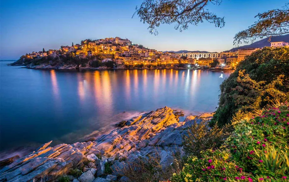 Baia illuminata al crepuscolo a Samos, con riflessi dorati sull’acqua e vegetazione rigogliosa.