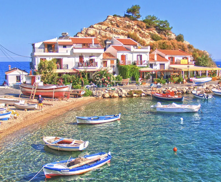 Port de pêche pittoresque d’Ireon à Samos, avec bateaux traditionnels et maisons blanches au pied d’une colline rocheuse.