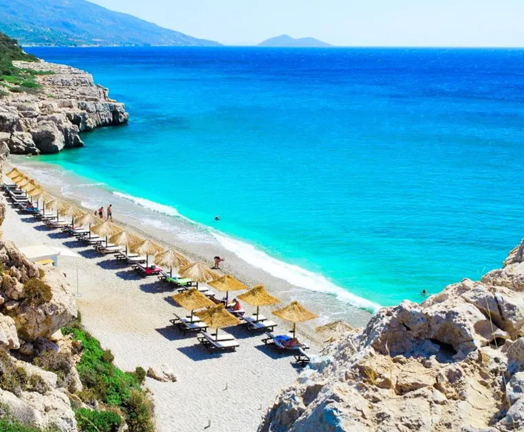 Plage de sable doré à Marathokambos, Samos, avec parasols en paille et eau turquoise étincelante.