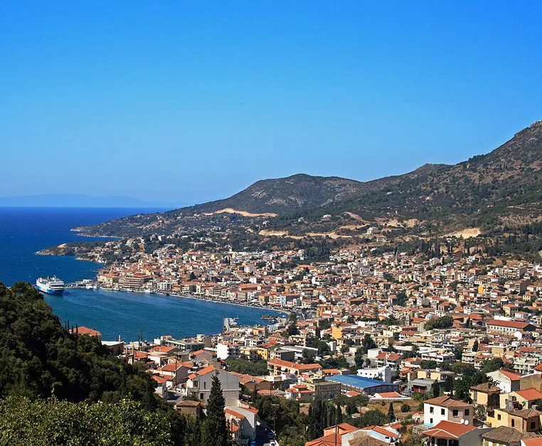 Vue panoramique du port de Samos à Vathi, avec ses bâtiments colorés et la mer Égée sous un ciel bleu clair.