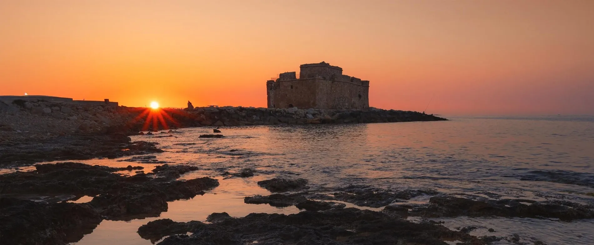 Sunset over Paphos Castle and rocky shoreline with calm sea in Cyprus.