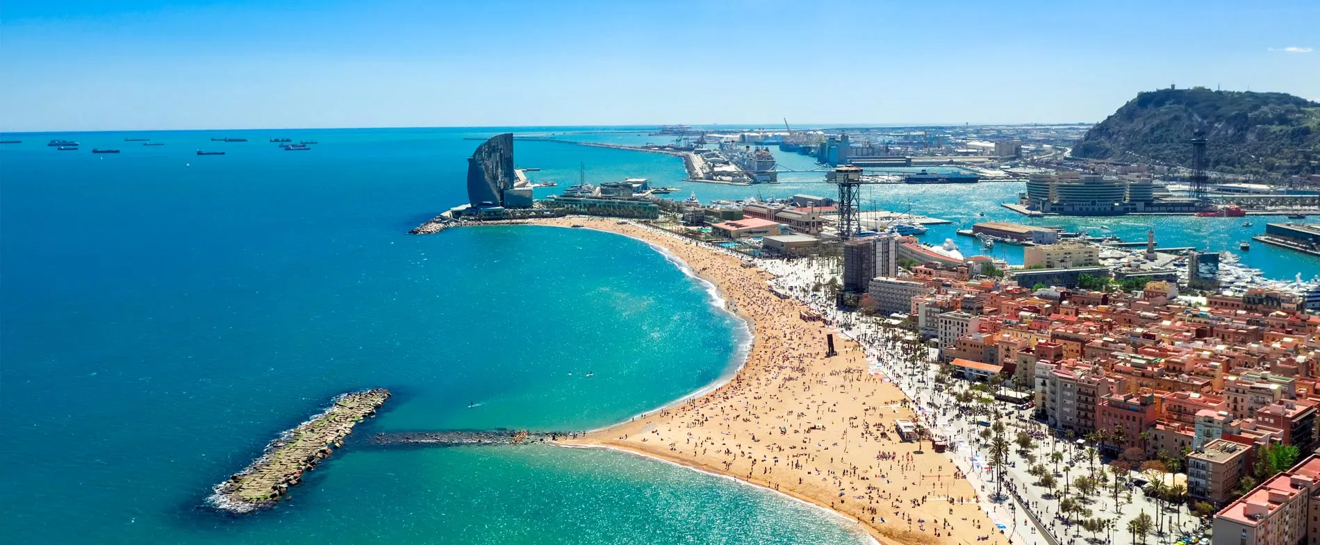 Coasta Barcelonei cu plajă aglomerată și port, ideală pentru închirierea mașinilor pe coasta mediteraneană.