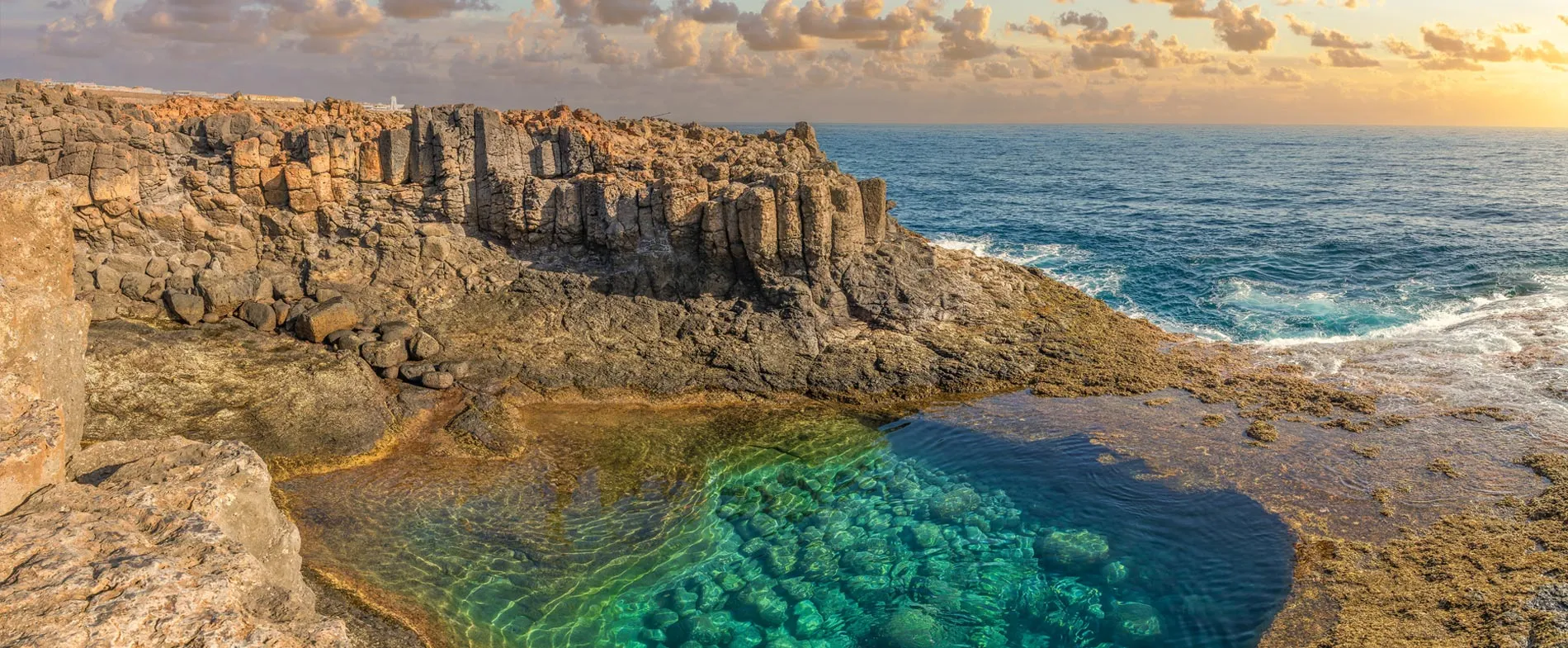 Rocky coastline with clear turquoise water and a sunset sky by the ocean.