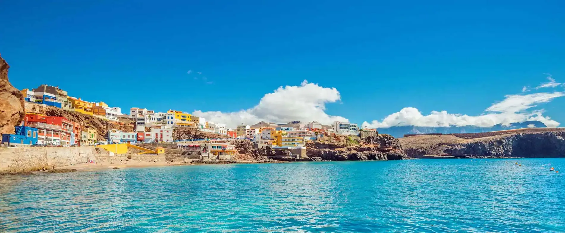 Coastal town with colorful buildings on cliffs above calm blue sea under a clear sunny sky.