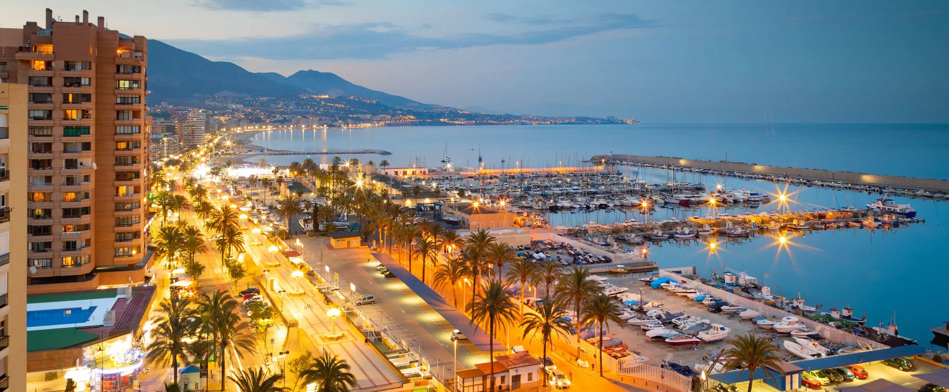 Coasta Alicante la amurg, cu marină, mașini, palmieri și străzi iluminate pe malul apei.