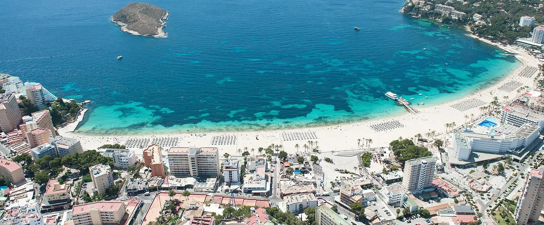 Palma de Mallorca beach with clear blue sea and urban buildings along the coastline for car rental.