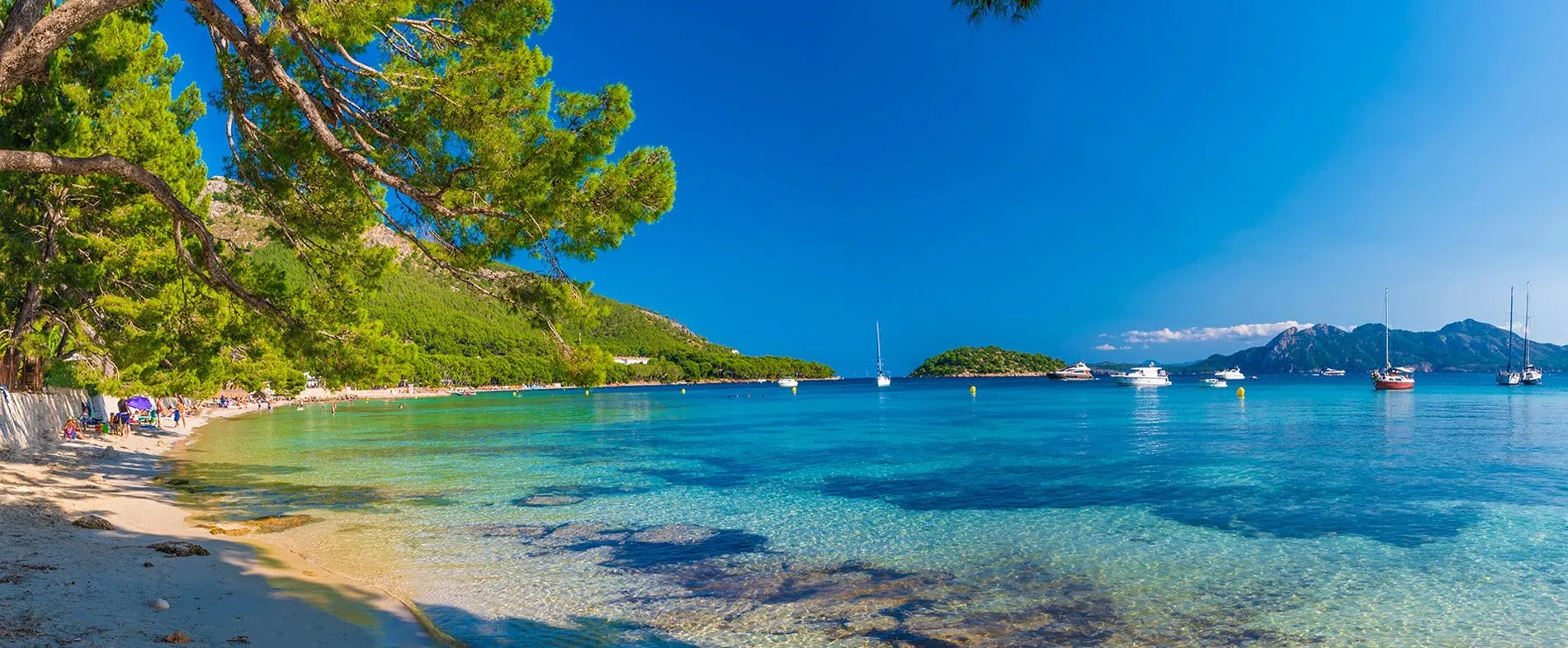 Sea and beach at Port de Pollenca with clear water and boats anchored near the shore in Mallorca, Spain.