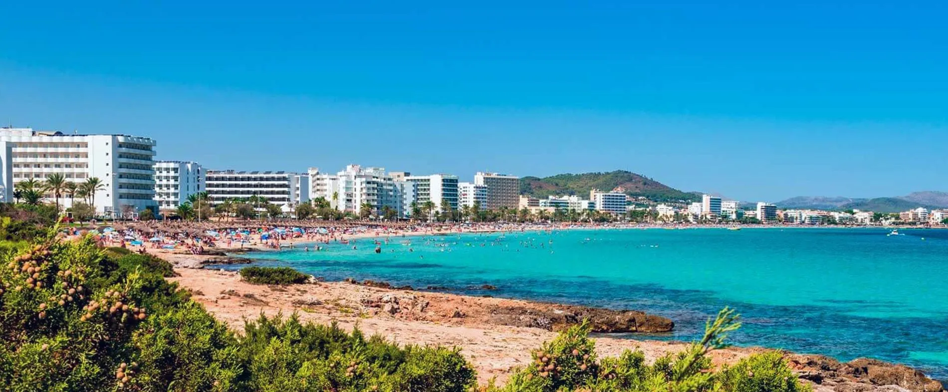 Spiaggia Playa d'en Bossa a Ibiza con acqua turchese e spiaggia affollata con edifici sullo sfondo.