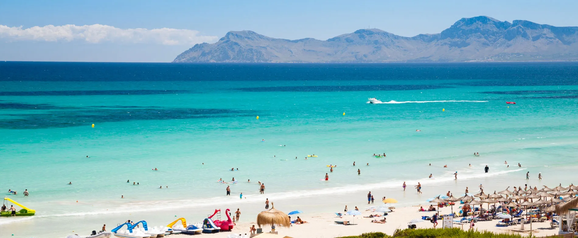 Sunny beach in Mallorca with turquoise waters, people swimming, and umbrellas along the sandy shore.