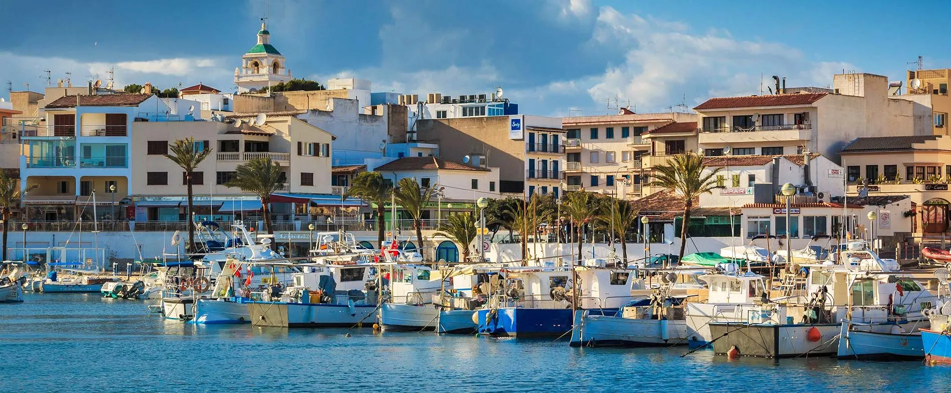 Porto di Calvià con barche attraccate e edifici mediterranei sullo sfondo in una giornata di sole.