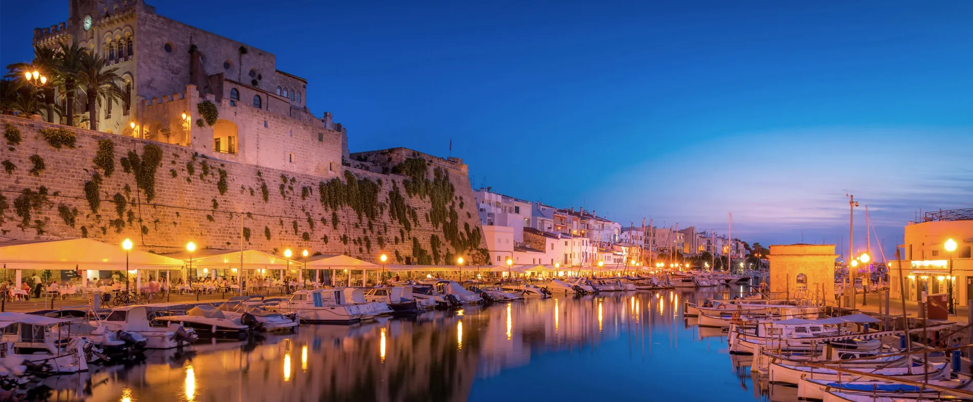 Port de Ciutadella à Minorque au crépuscule avec bateaux et restaurants illuminés.