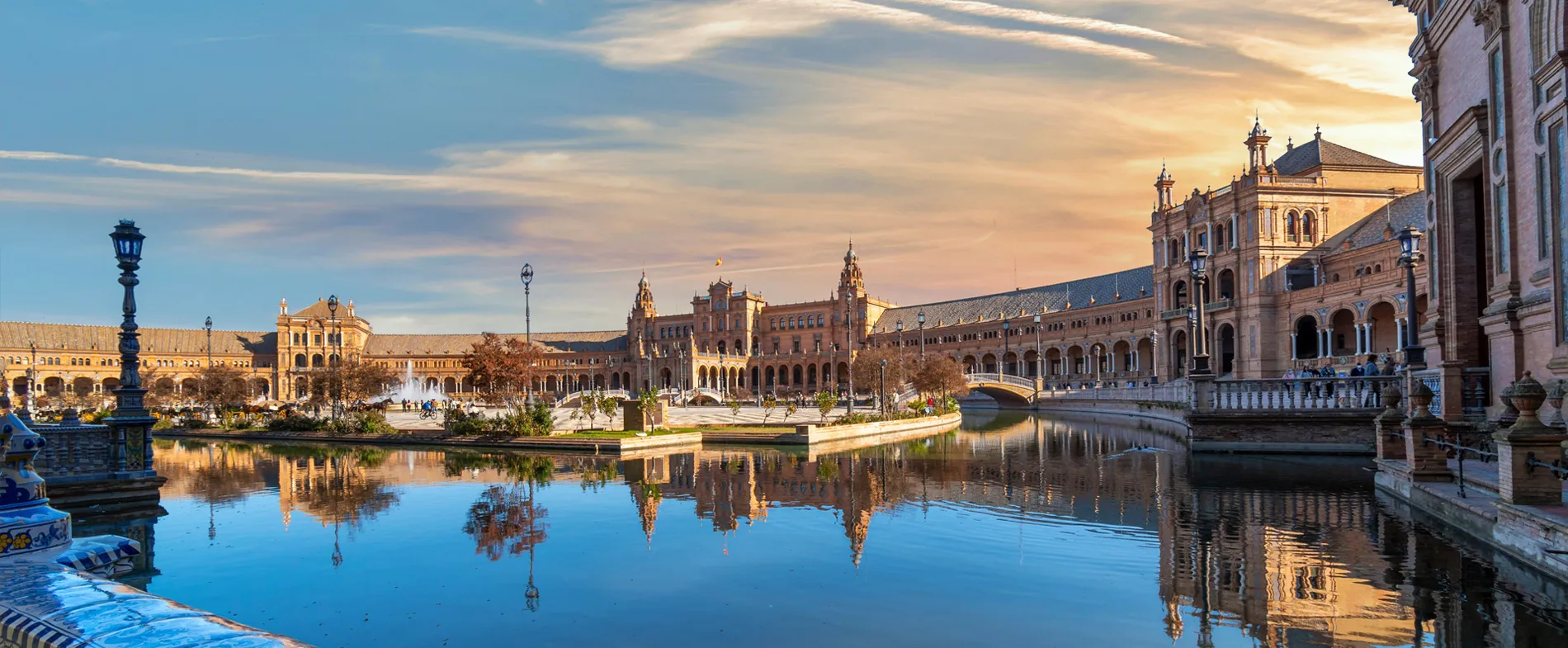Piața Spaniei din Sevilla cu arhitectură istorică și canal sub un cer luminos la apus.