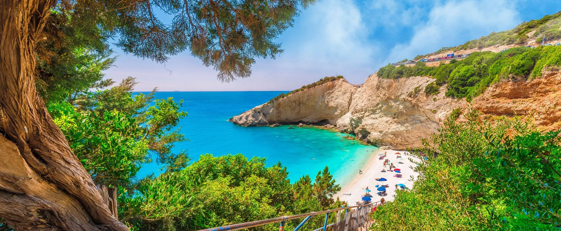 Spiaggia di Myrtos a Cefalonia con acque turchesi, scogliere rocciose e ombrelloni sulla spiaggia.