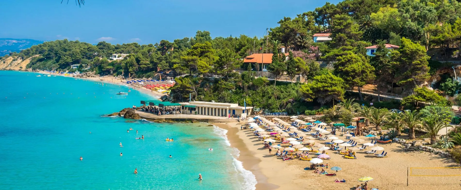Sithonia beach in Halkidiki with sunbeds, umbrellas, and people swimming in clear blue water.