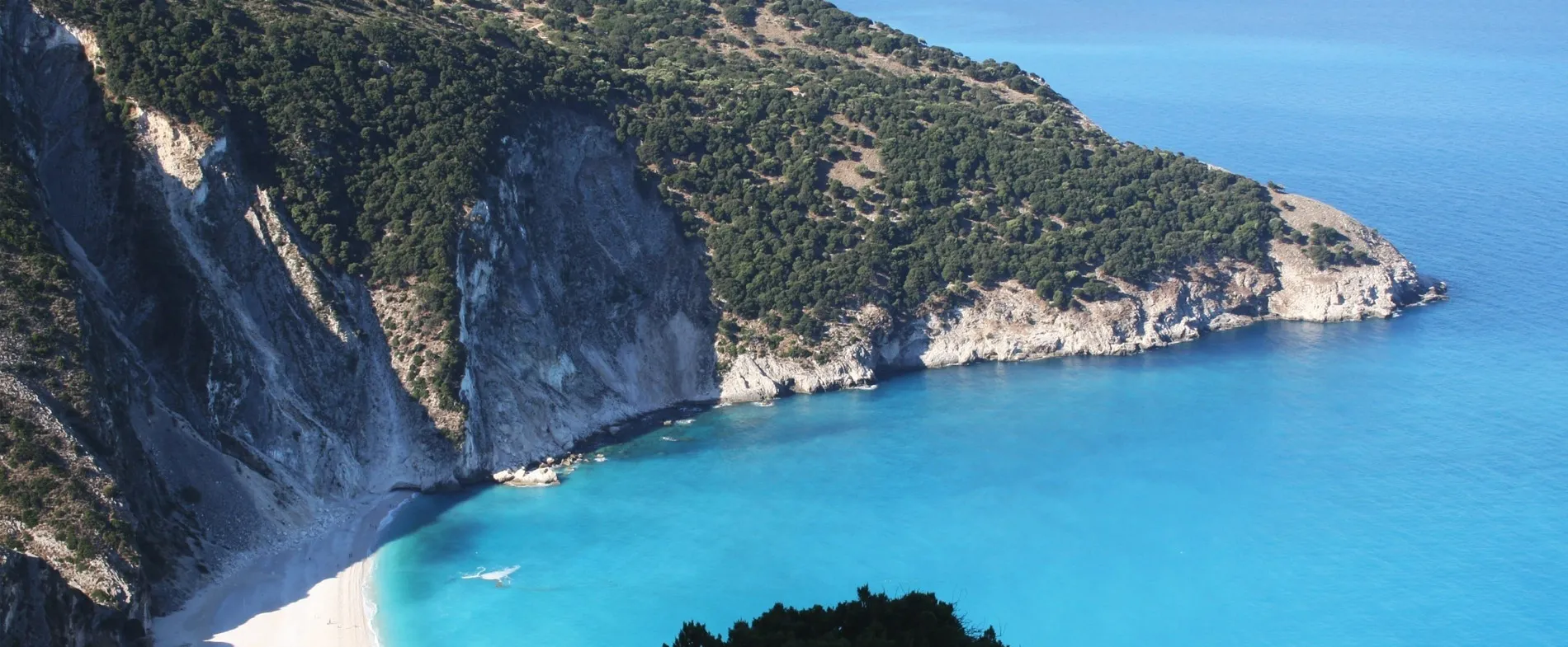 Myrtos Beach coastline with clear turquoise water and lush green hills in Greece.