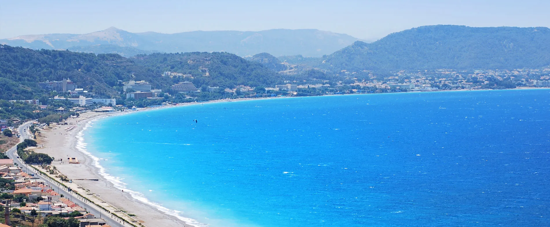 Rhodes coast with blue sea, beach, and hills in the background on a sunny day.