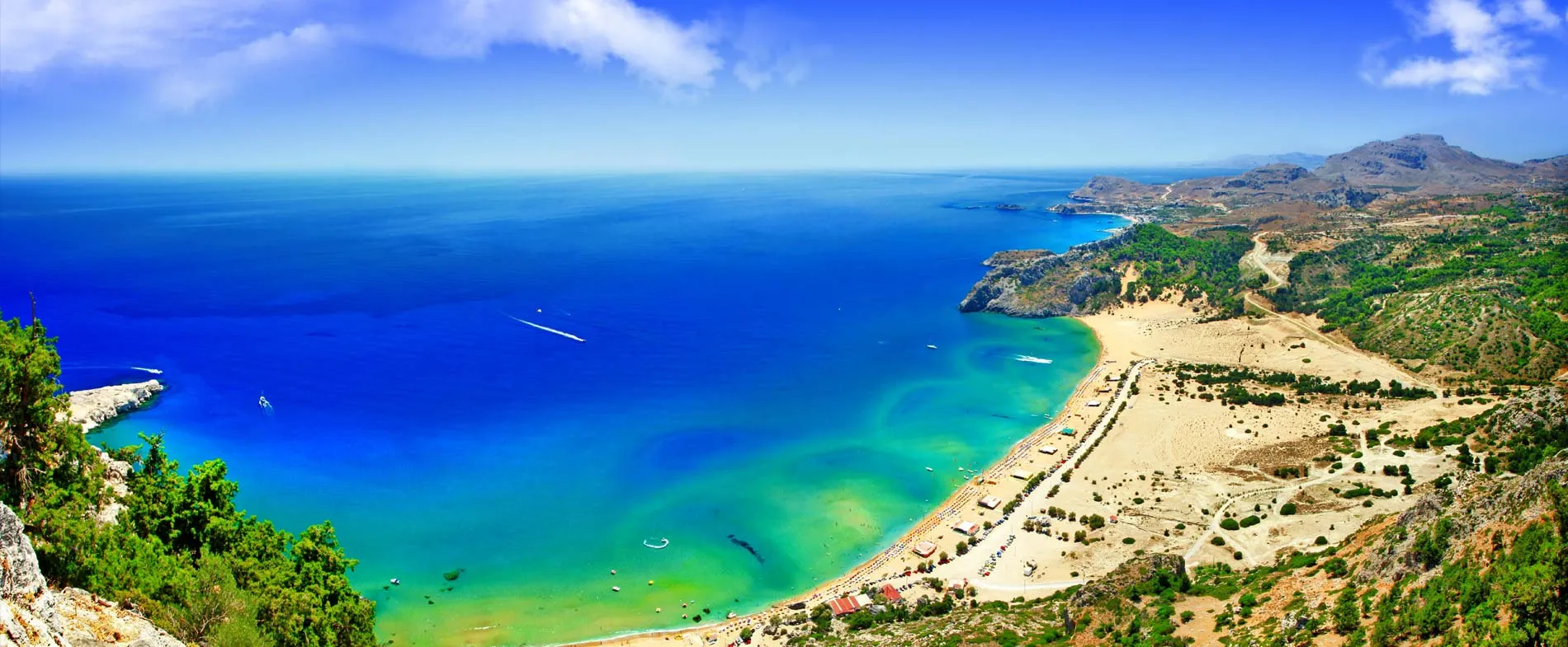 Lindos beach and coastline with clear blue sea and sandy shore under a sunny sky in Rhodes, Greece.