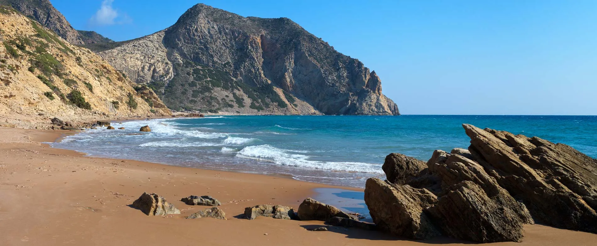 Red beach in Crete with sandy shore, clear blue sea, and rocky cliffs under a bright sky.