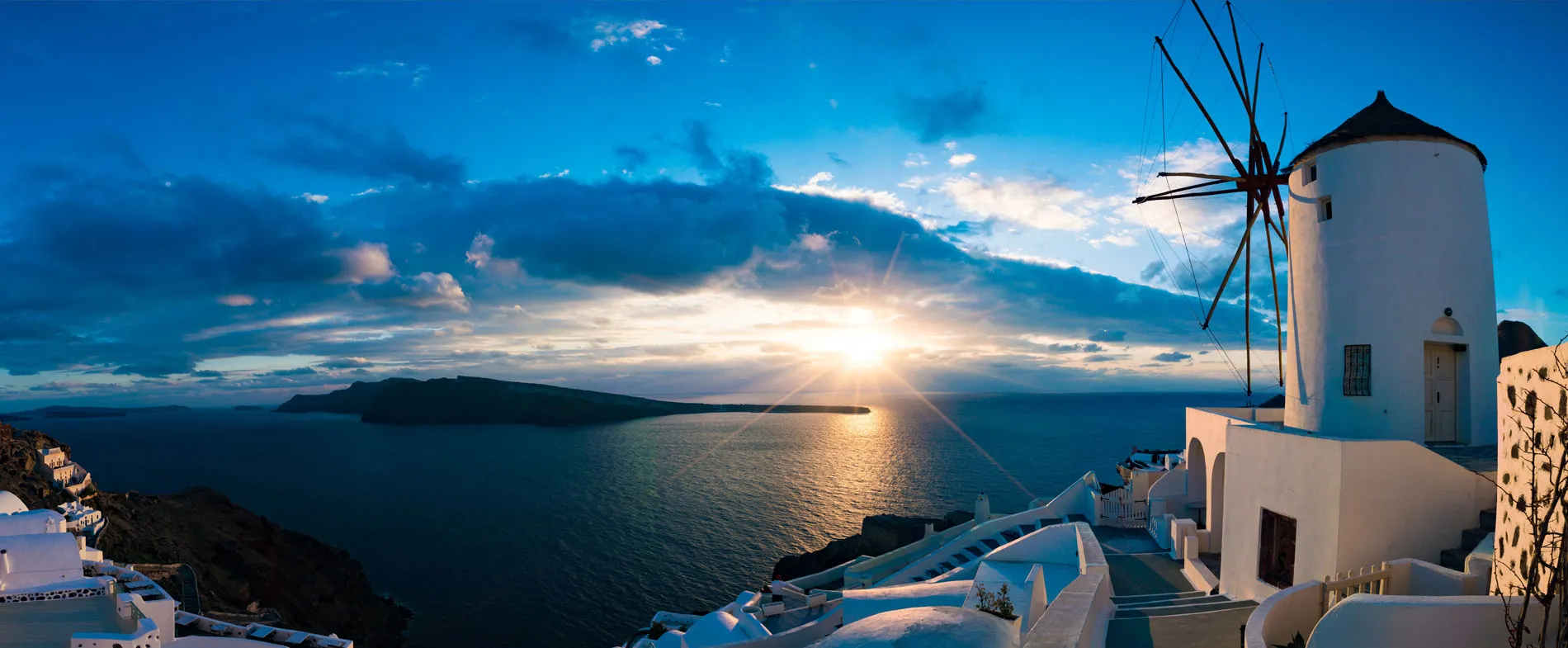 Santorini island view with iconic white windmill overlooking caldera at sunset in Greece.