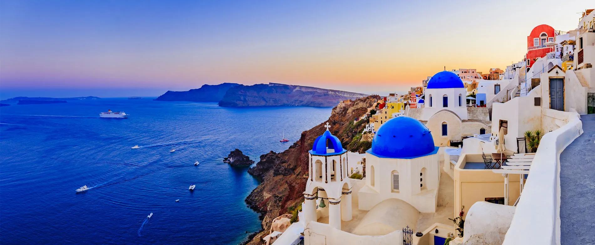Santorini coastline at sunset with blue-domed churches and boats in the sea, perfect for car rental trips.
