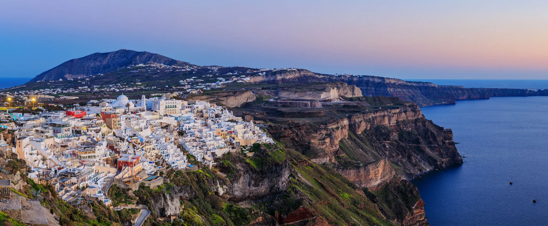Santorini town with white buildings on cliffs by the sea at sunset, ideal for car rental vacations.