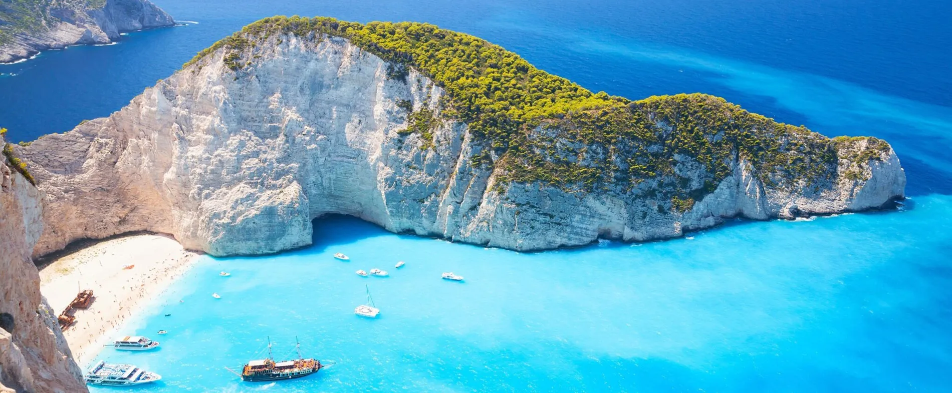 Spiaggia di Navagio a Zante con acqua turchese, barche e insenatura sabbiosa tra scogliere ripide.