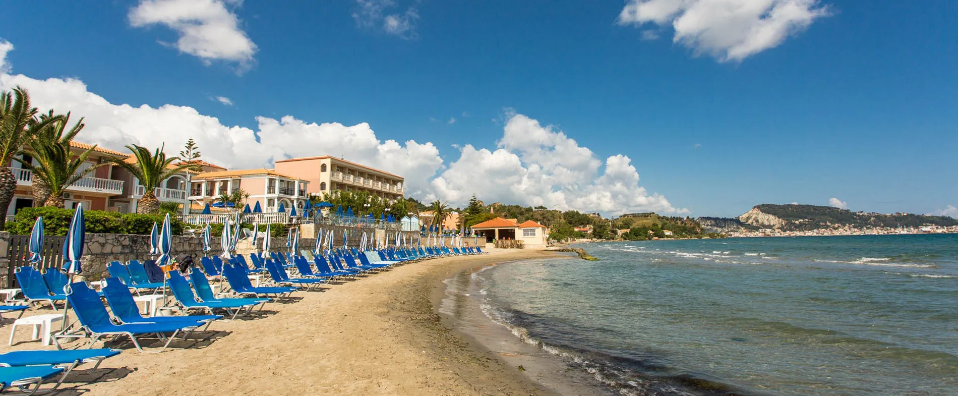 Sandy beach with blue sun loungers and umbrellas by the sea under a clear sky.