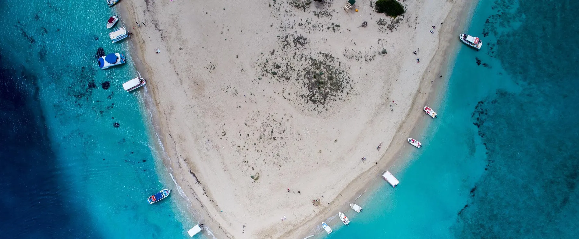 Sandy beach with small boats docked along the clear blue water shore.