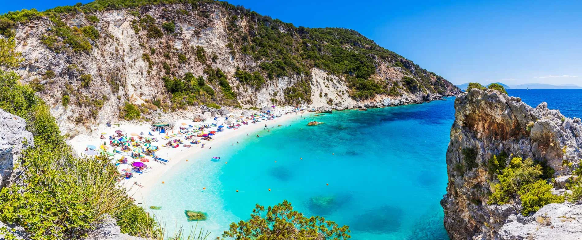 Myrtos Beach in Kefalonia with turquoise waters, rocky cliffs, and colorful umbrellas on the sandy shore.