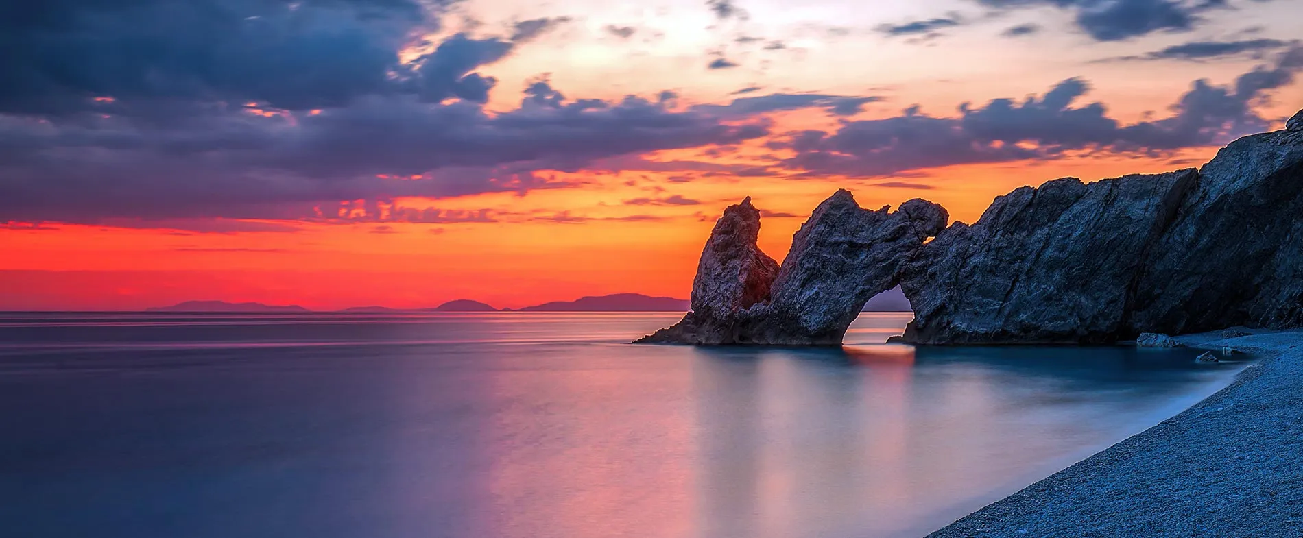 Tramonto sul mare tranquillo con formazioni rocciose uniche su una spiaggia costiera tranquilla.