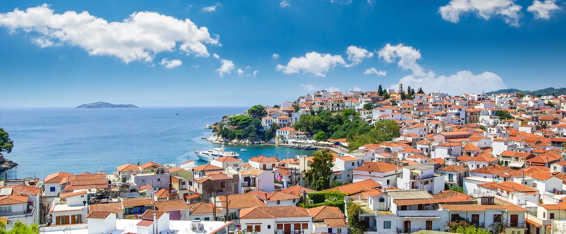 Stadt Skiathos mit weißen Gebäuden und Terrakottadächern am blauen Meer an einem sonnigen Tag.