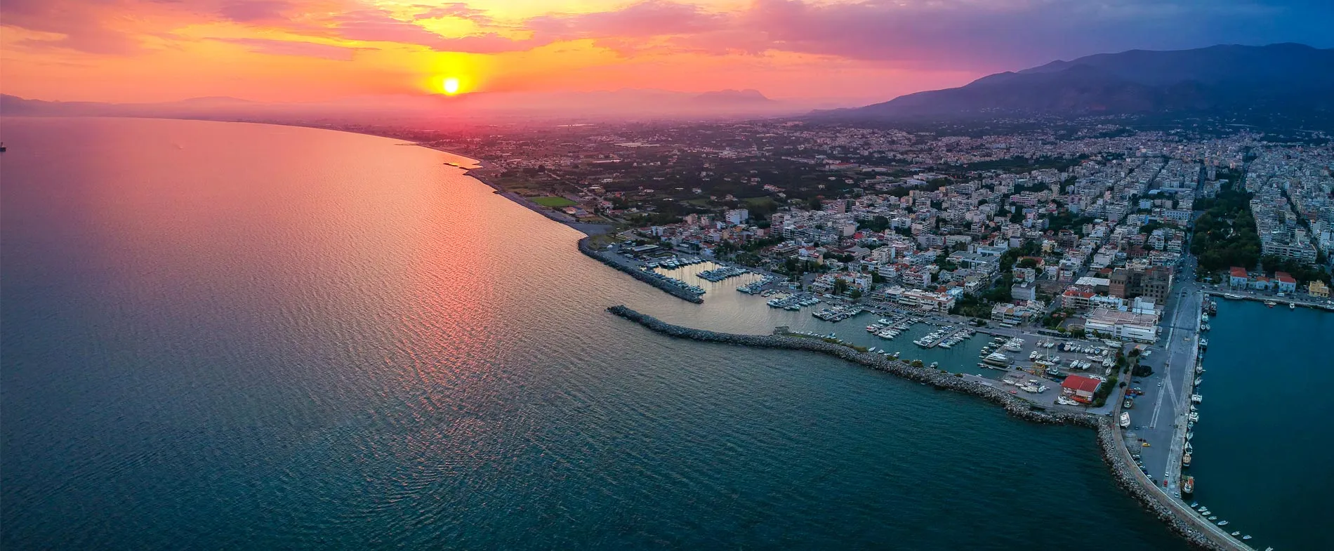 Costa di Patrasso al tramonto con marina e edifici della città sotto un cielo colorato.