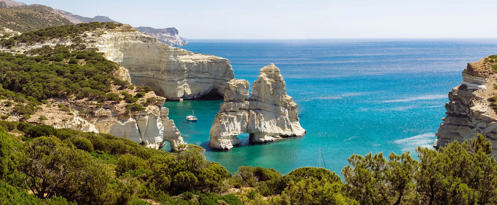 Milos island coast with clear turquoise sea, white rock formations, and boats near the shore.