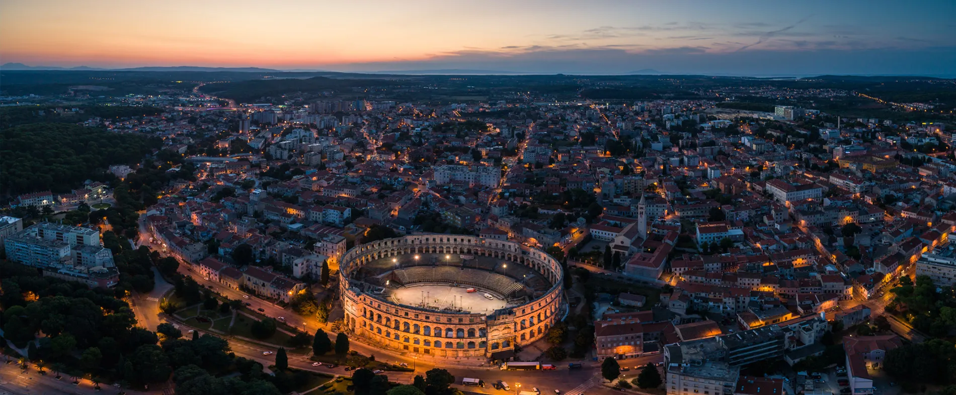 Pula cityscape at dusk with the ancient Roman amphitheater illuminated in the foreground.