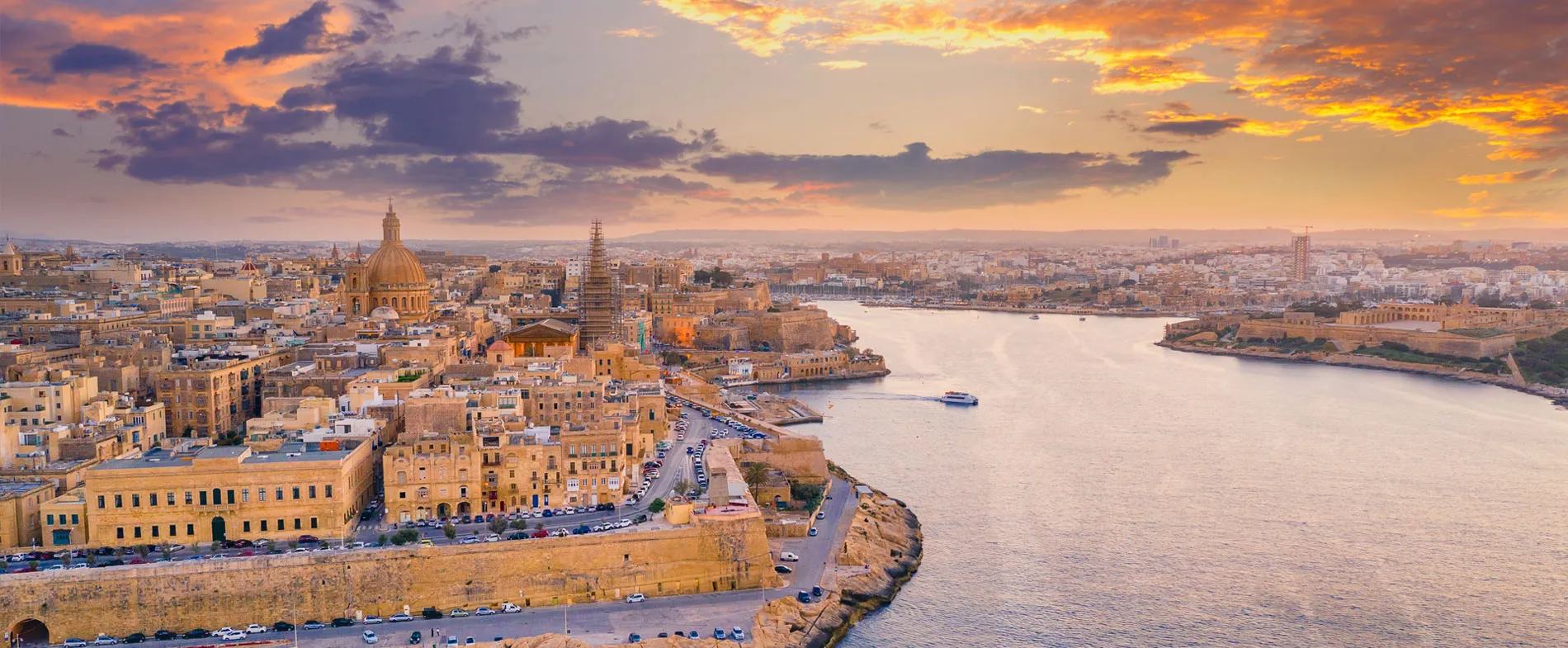 Panoramic view of Valletta, Malta at sunset with historic buildings along the waterfront and calm sea.