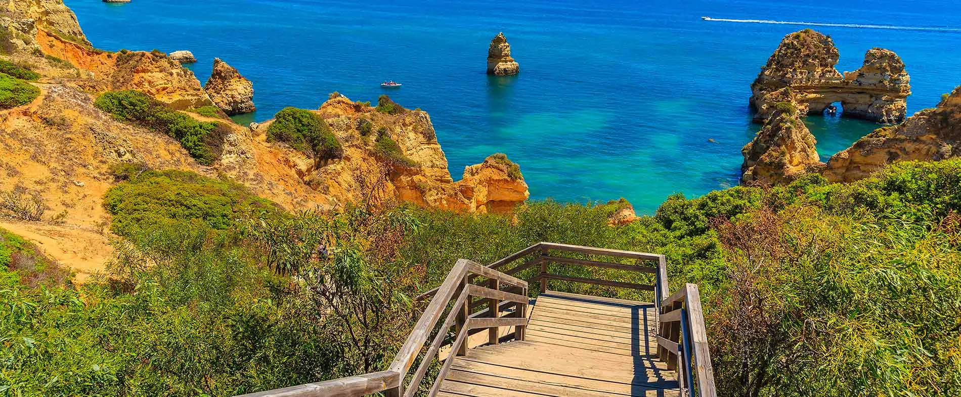 Wooden stairs lead down to the turquoise sea and rocky cliffs at Algarve's scenic coastline in Portugal.