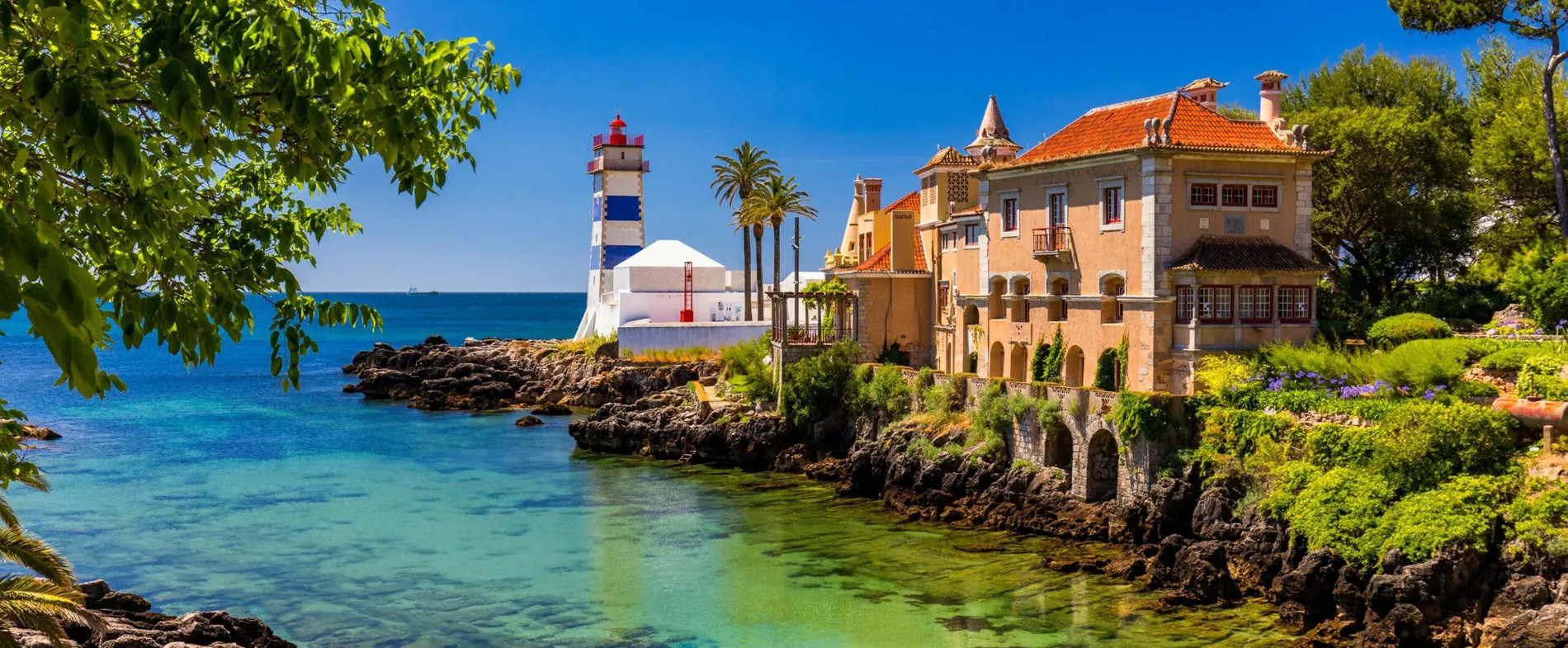 Seaside view of the Boca do Inferno lighthouse and estate in Cascais, Portugal with clear blue water and greenery.
