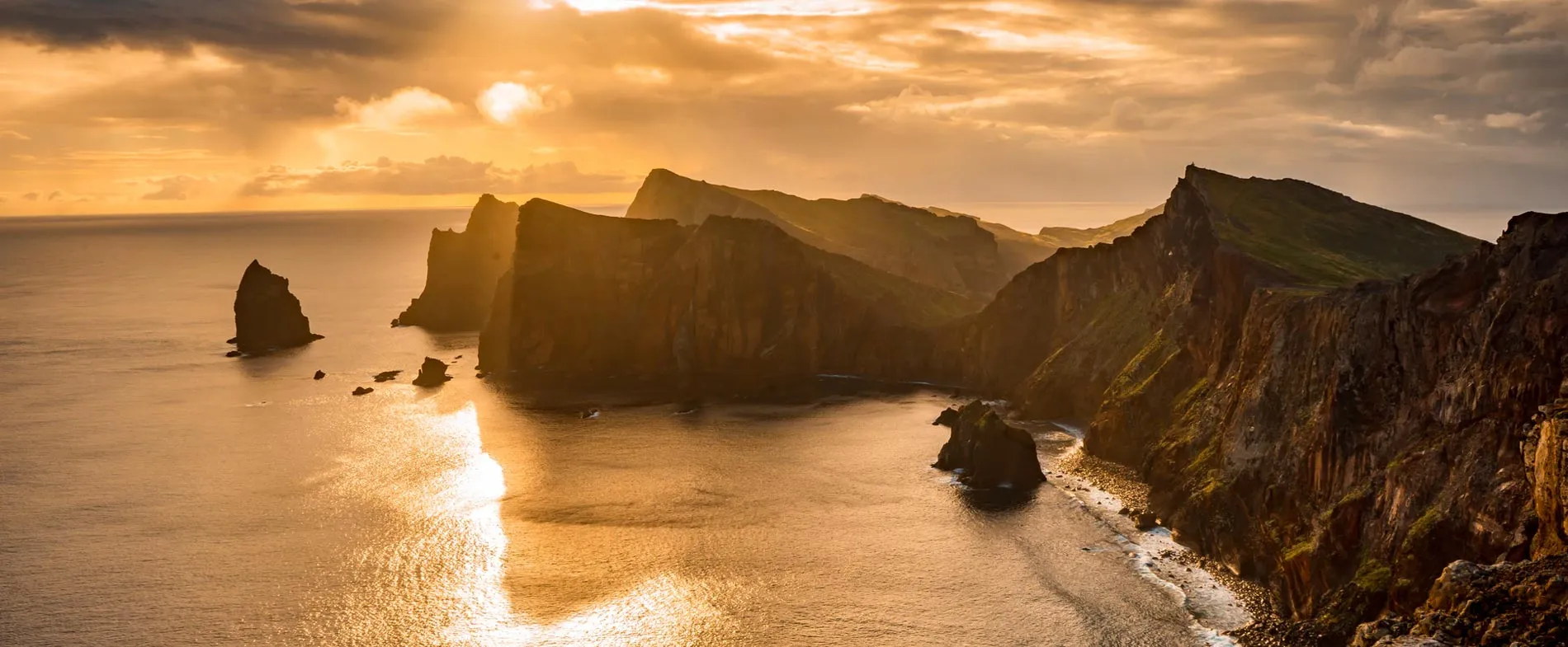 Sunset view over rocky cliffs and calm sea along a rugged coastline for travel and car rental inspiration.