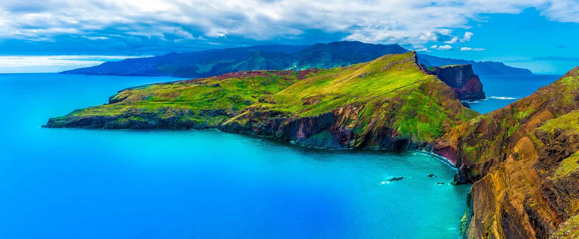 Madeira coastline with vibrant green cliffs and clear blue ocean under a partly cloudy sky for car rental trips.