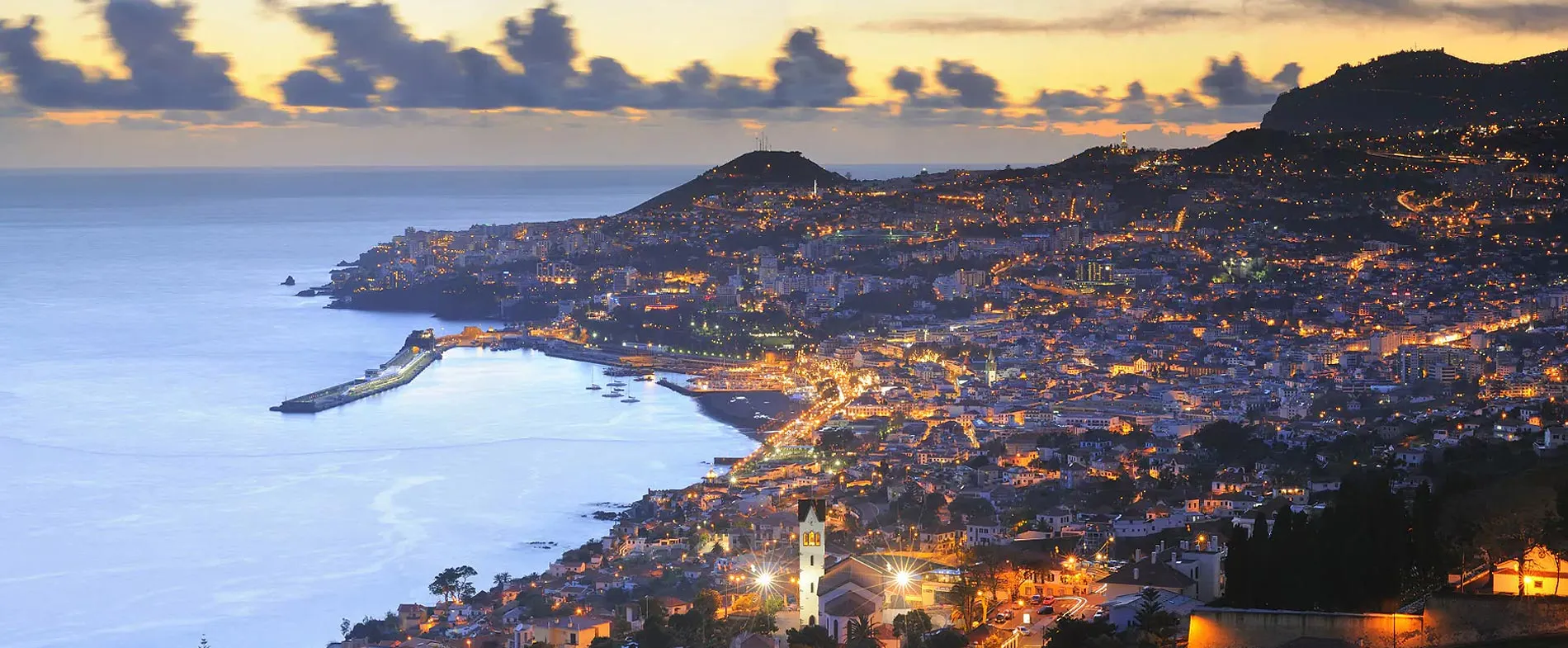 Madeira coastline at sunset with city lights and coastal bay near ocean water.