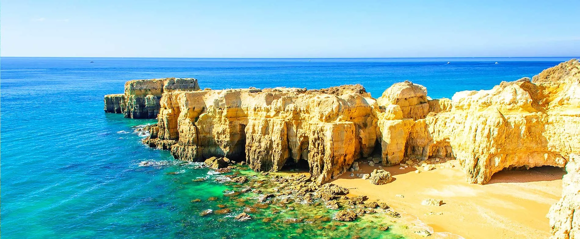 Algarve coastline with rocky cliffs and clear blue sea under a bright sky.