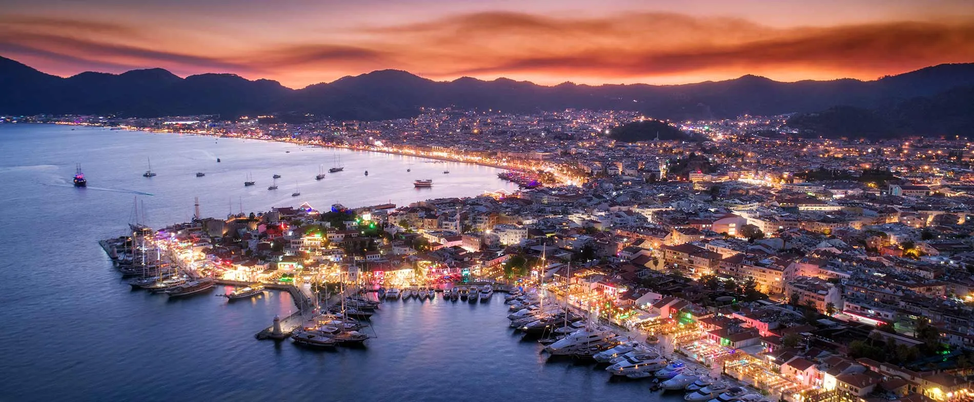 Marmaris kıyısı, gün batımında aydınlatılmış liman ve demirlemiş teknelerle.