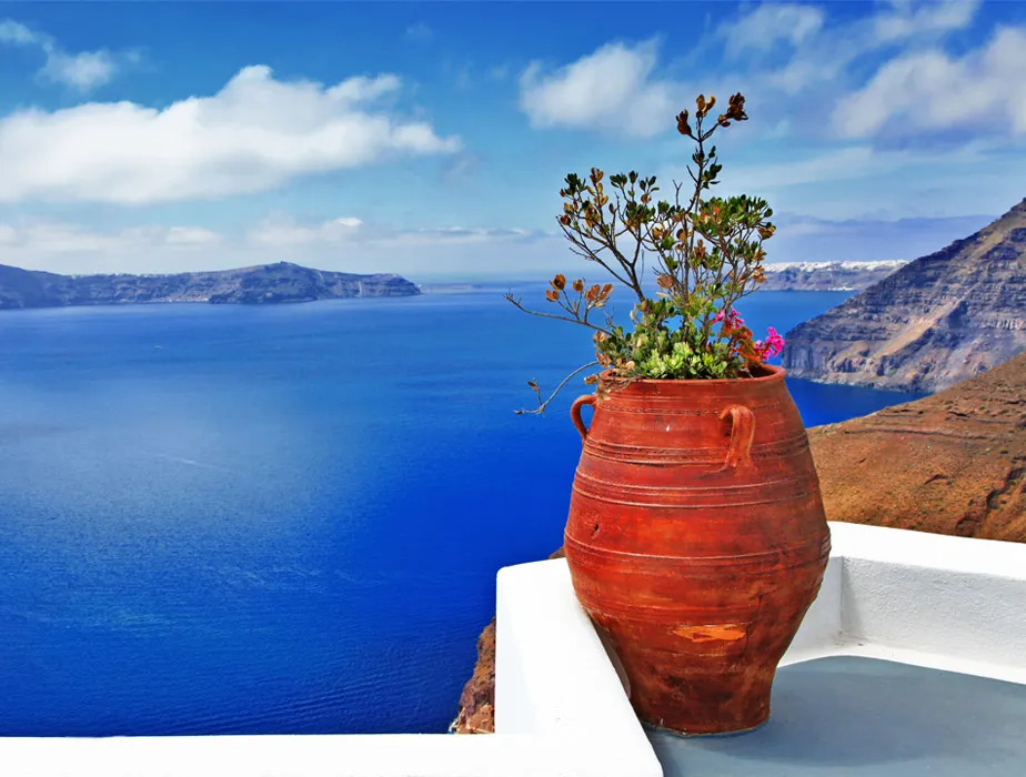 Santorini sea view with a clay pot and plant on a white terrace overlooking the caldera cliffs.