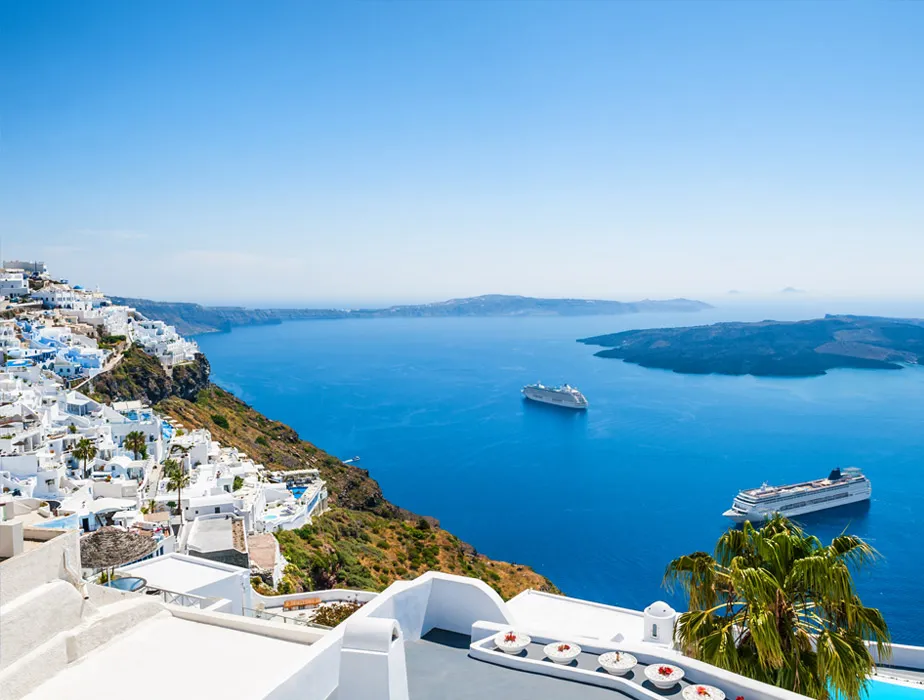 Santorini cliffside view with white buildings overlooking the deep blue sea and cruise ships for car rental trips.